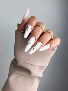 long white stiletto nails with minimalist wavy gold chrome lines and gold rings.