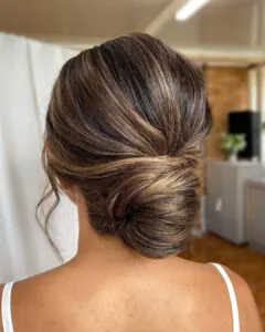 brunette woman showing a modern low chignon bridal hairstyle from the back.