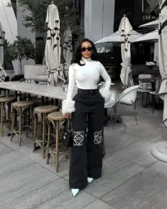 woman in white turtleneck with feathered cuffs and black wide leg jeans at an outdoor cafe