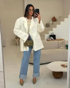 woman wearing an oversized white blazer and light blue jeans holding a small olive purse.