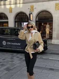 woman in a tan cropped trench coat and black capri pants walking on a city street.