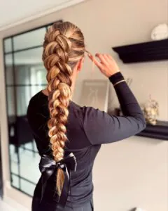 long blonde dutch braid tied with a black satin bow at the ends