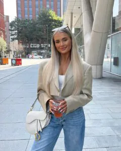 woman with long straight blonde hair wearing a blazer and holding a drink.