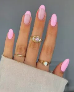 hand with pink french tip manicure and various gold gemstone rings