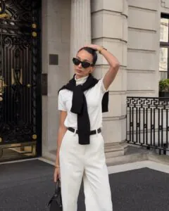 woman wearing white trousers and a black sweater over her shoulders in front of stone columns