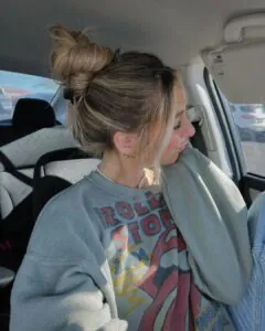 woman in a car with blonde hair styled in a high top knot.