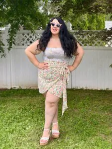 plus size woman in a floral wrap dress and white sunglasses posing in a garden