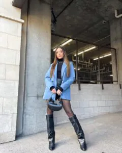 woman in blue blazer black turtleneck and leather boots holding a black purse
