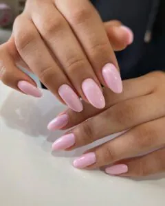 glossy baby pink almond shaped nails on a hand resting on a surface
