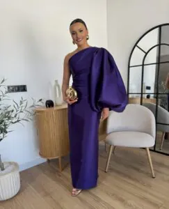 woman in purple one shoulder gown with dramatic puff sleeve holding gold clutch