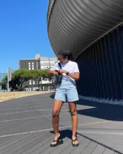woman wearing white t-shirt, light blue denim shorts, and black platform flip flops.