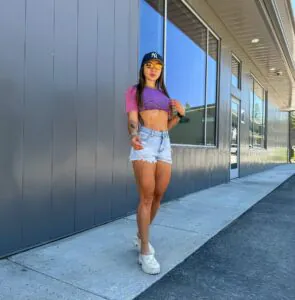 woman in purple crop top, distressed denim shorts, and white platform clogs outdoors.