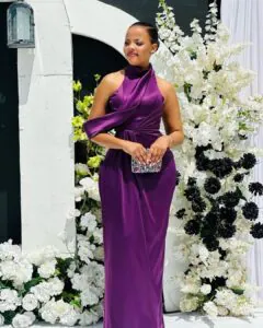 woman in high neck purple satin gown standing before a white floral backdrop