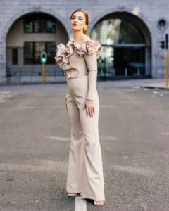 woman in beige off-the-shoulder jumpsuit with floral 3d embellishments standing on a street