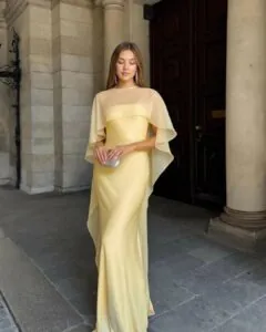 woman in long butter yellow gown with sheer cape overlay standing by stone pillars