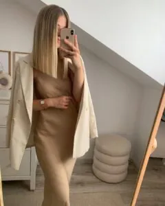 woman in beige satin slip dress and matching oversized blazer taking a mirror selfie