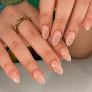 almond shaped nude nails featuring iridescent glitter and delicate white wavy lines