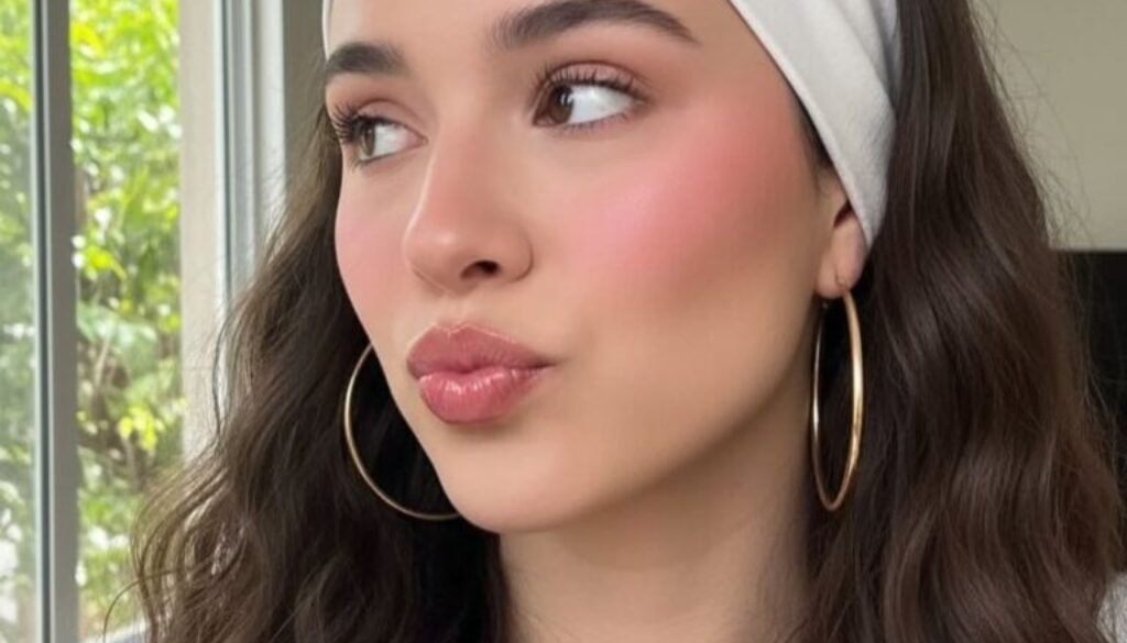 woman with long wavy brown hair wearing a wide white fabric headband and gold hoop earrings.