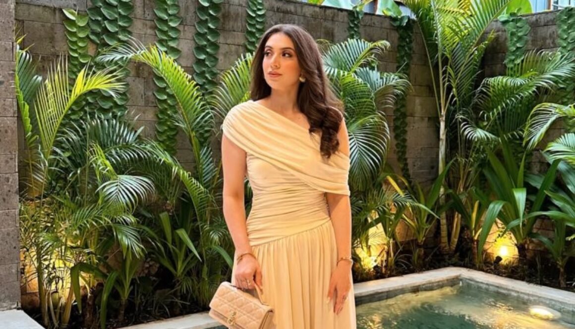 woman in cream off-the-shoulder maxi dress standing by tropical pool with lush greenery