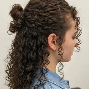 side view of a young woman with curly brown hair styled in a half-up bun.