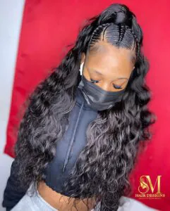 woman with long dark wavy hair in a half-up ponytail with small scalp braids.