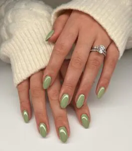 sage green oval nails on hands wearing a white cable knit sweater and rings