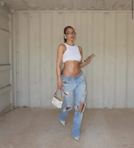 woman in white crop top and ripped light blue jeans holding small purse