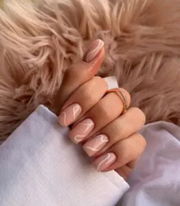 nude square nails with white swirl designs resting on a pink faux fur surface