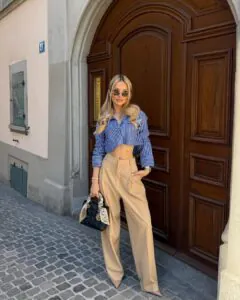 woman in a blue striped cropped shirt and tan trousers standing by a wooden door