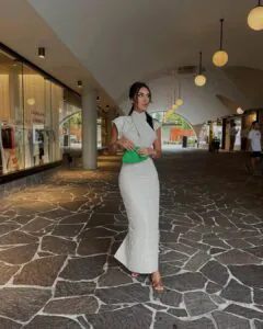 woman in a neutral linen maxi dress carrying a green clutch in an outdoor walkway.