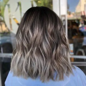 back view of a shoulder length wavy ash bronde balayage hairstyle with dark roots