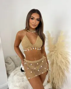 woman wearing a tan crochet two piece resort set with seashell accents and matching necklace
