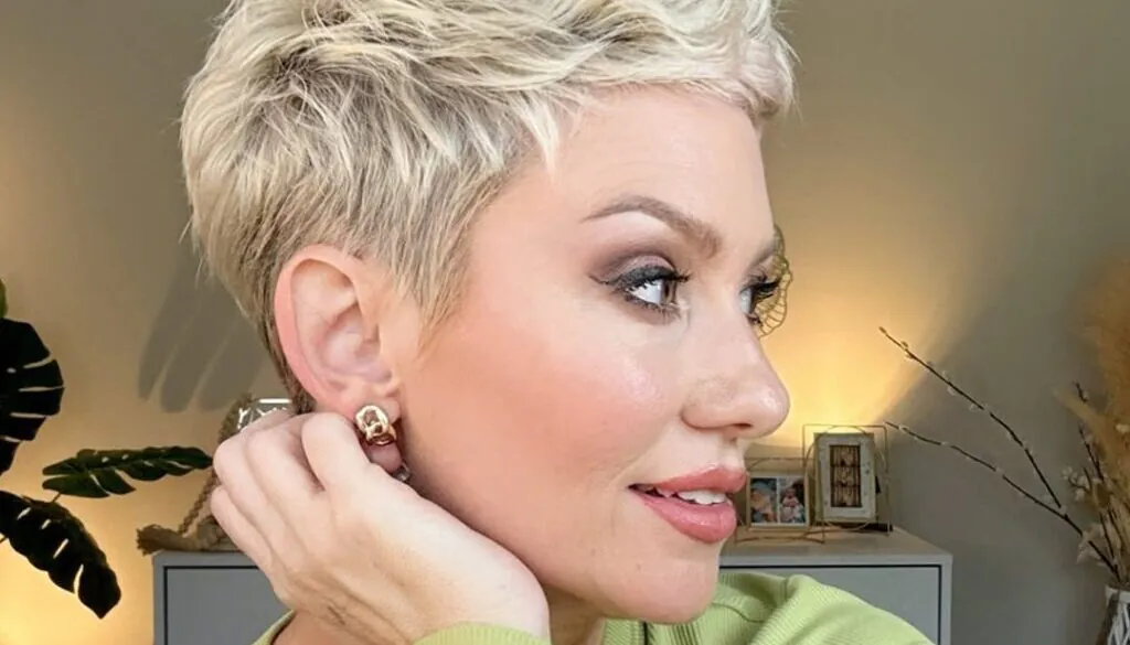 woman with a blonde spiky pixie cut looking sideways in a green shirt