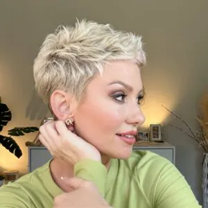 woman with a blonde spiky pixie cut looking sideways in a green shirt