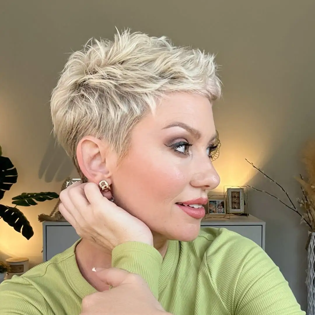 woman with a blonde spiky pixie cut looking sideways in a green shirt