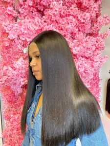 woman with long sleek black hair standing against a pink floral background