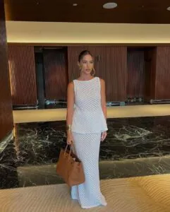 woman in white sleeveless crochet top and matching maxi skirt holding brown leather tote