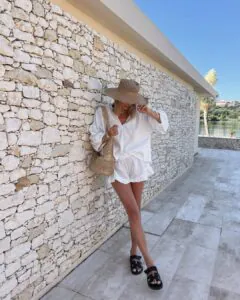 woman in white linen set and straw hat by stone wall