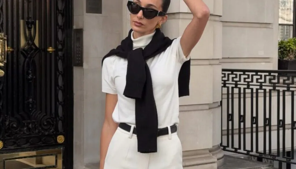 woman wearing white trousers and a black sweater over her shoulders in front of stone columns