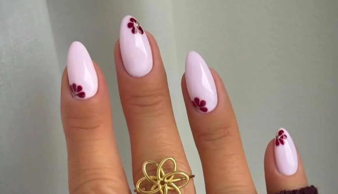 long almond pale pink nails with small maroon flower nail art and gold ring.