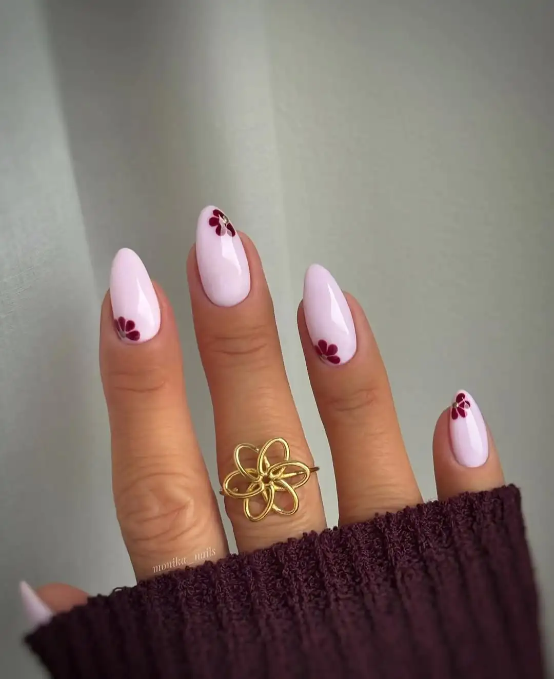 long almond pale pink nails with small maroon flower nail art and gold ring.