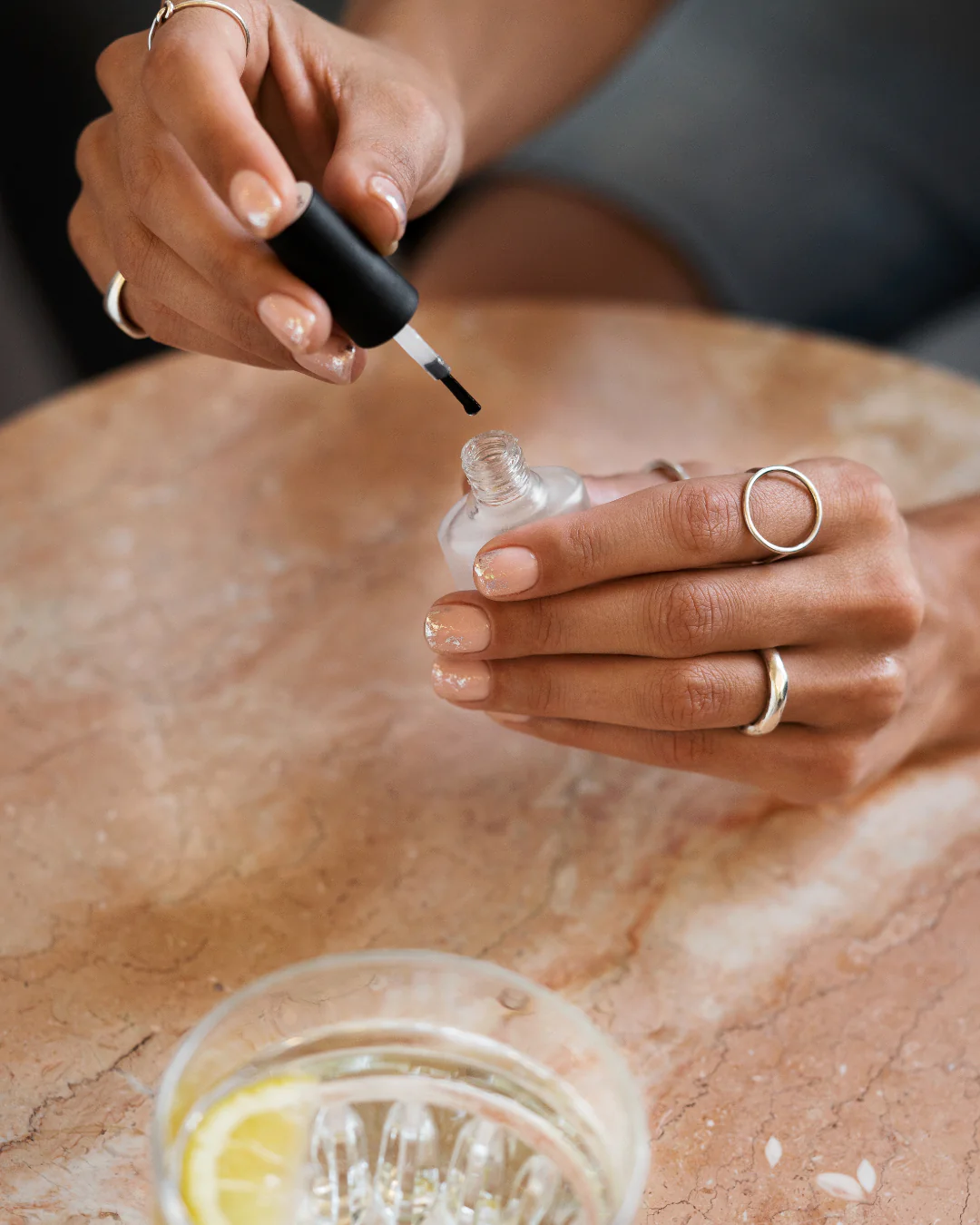 hands with silver rings holding a nail polish brush over a clear bottle