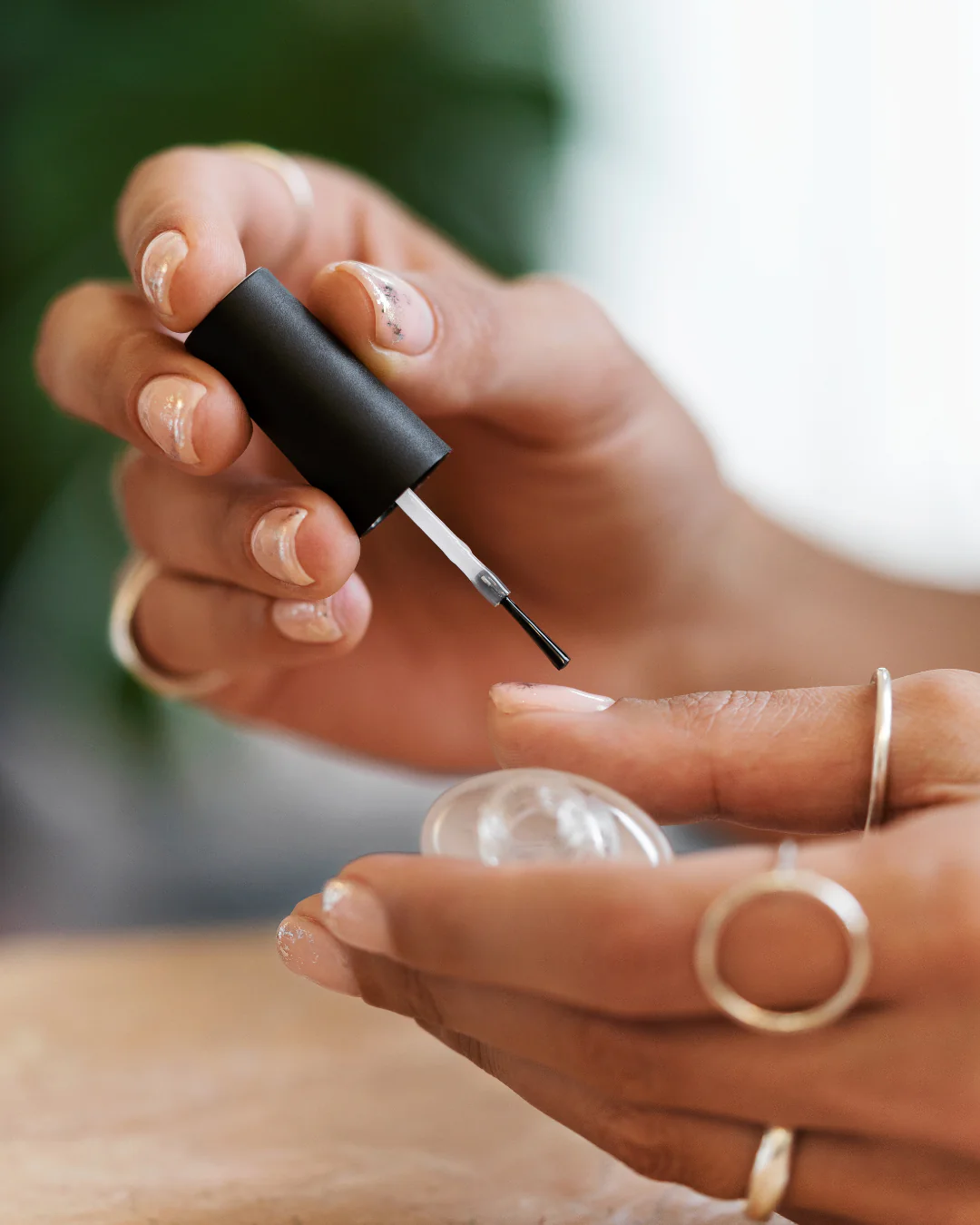 close up of hands with silver rings applying clear top coat nail polish