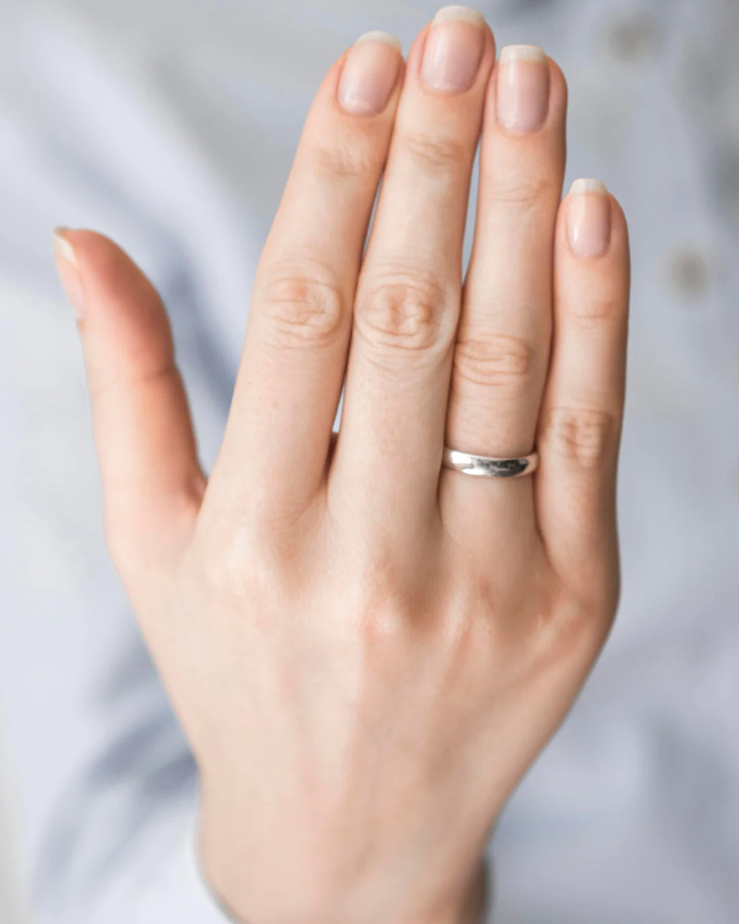 close up of a hand wearing a simple silver wedding band on the ring finger