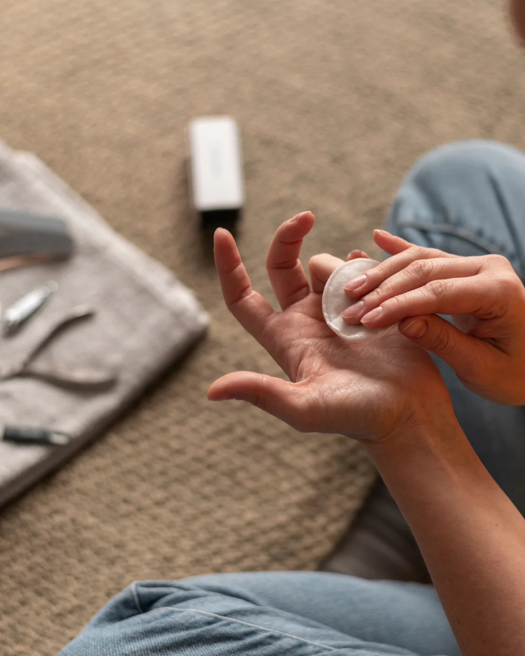 person using a cotton pad to clean nails with manicure tools nearby