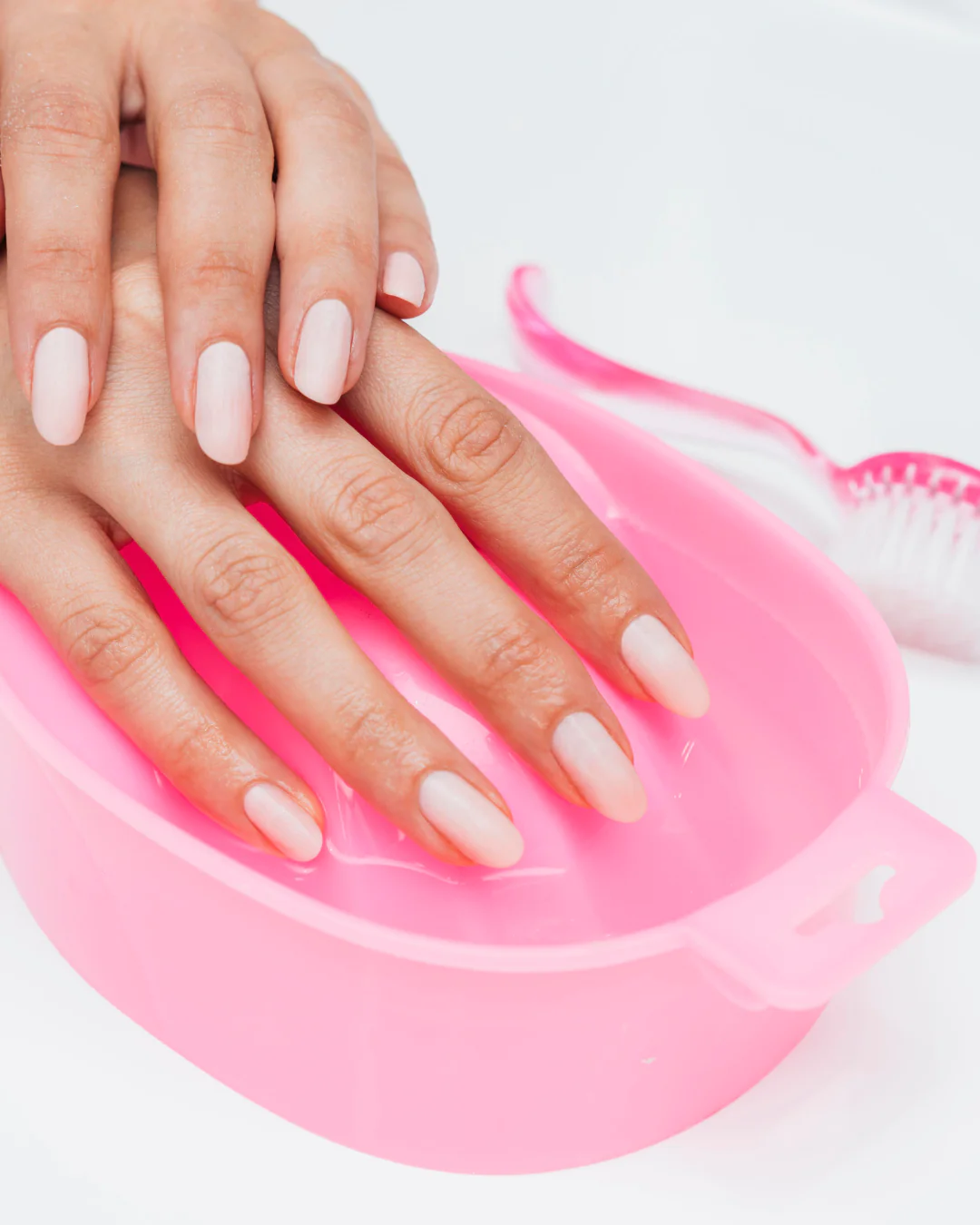 hands with light pink manicure soaking in a pink water bowl for treatment
