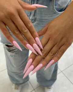 extra long baby pink stiletto nails on a person wearing light denim jeans