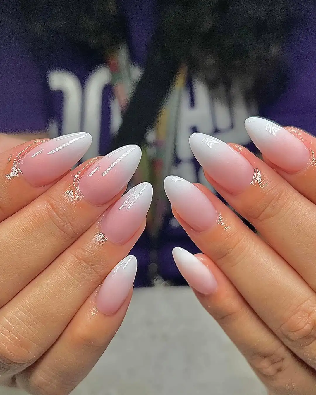 glossy pink and white ombre almond nails on a person with fair skin.