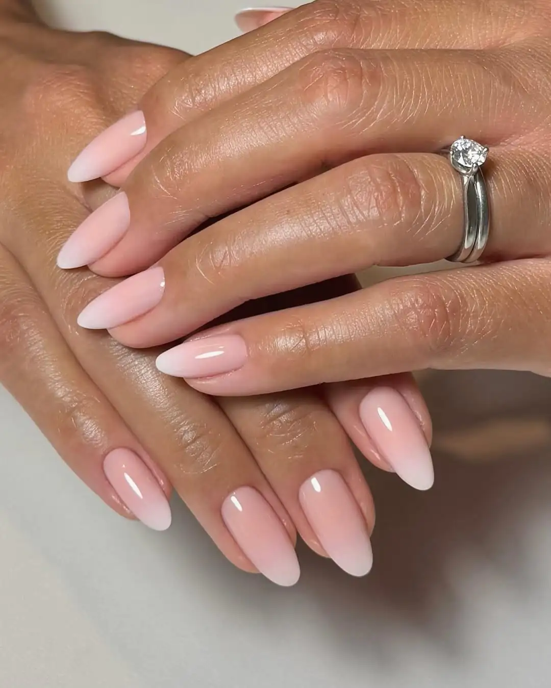 soft pink and white ombre almond nails on a hand wearing a diamond ring.