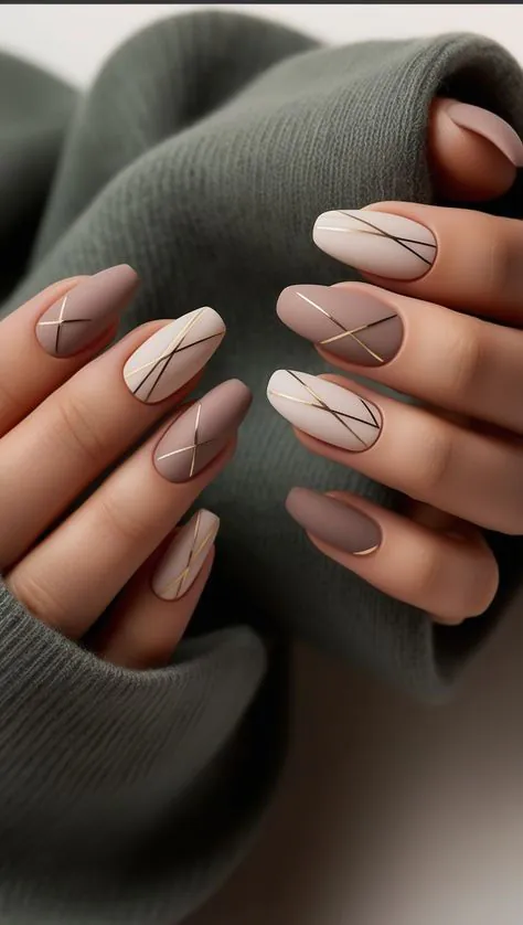 matte almond nails in taupe and cream with minimalist gold geometric line art.
